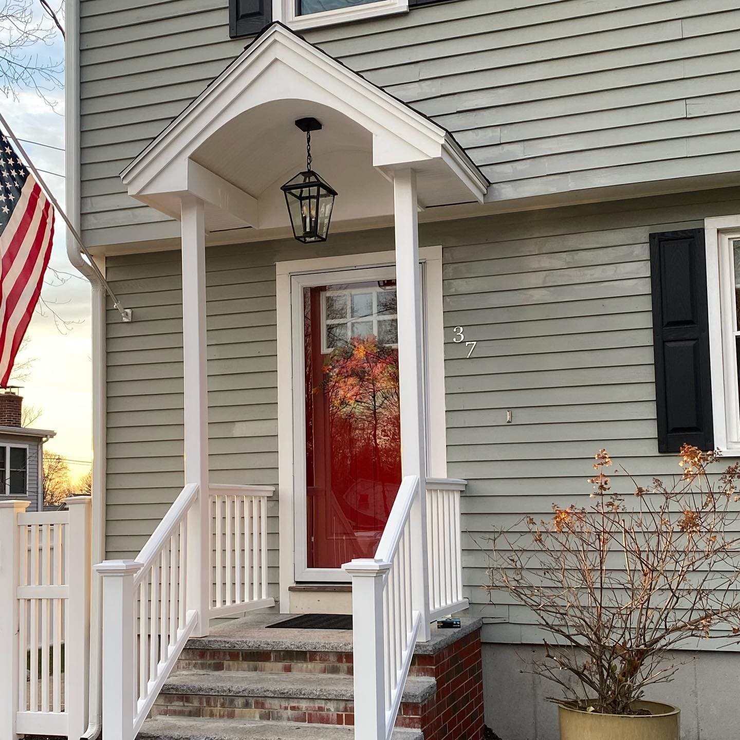 New front-entry portico with white columns, railings and a red door