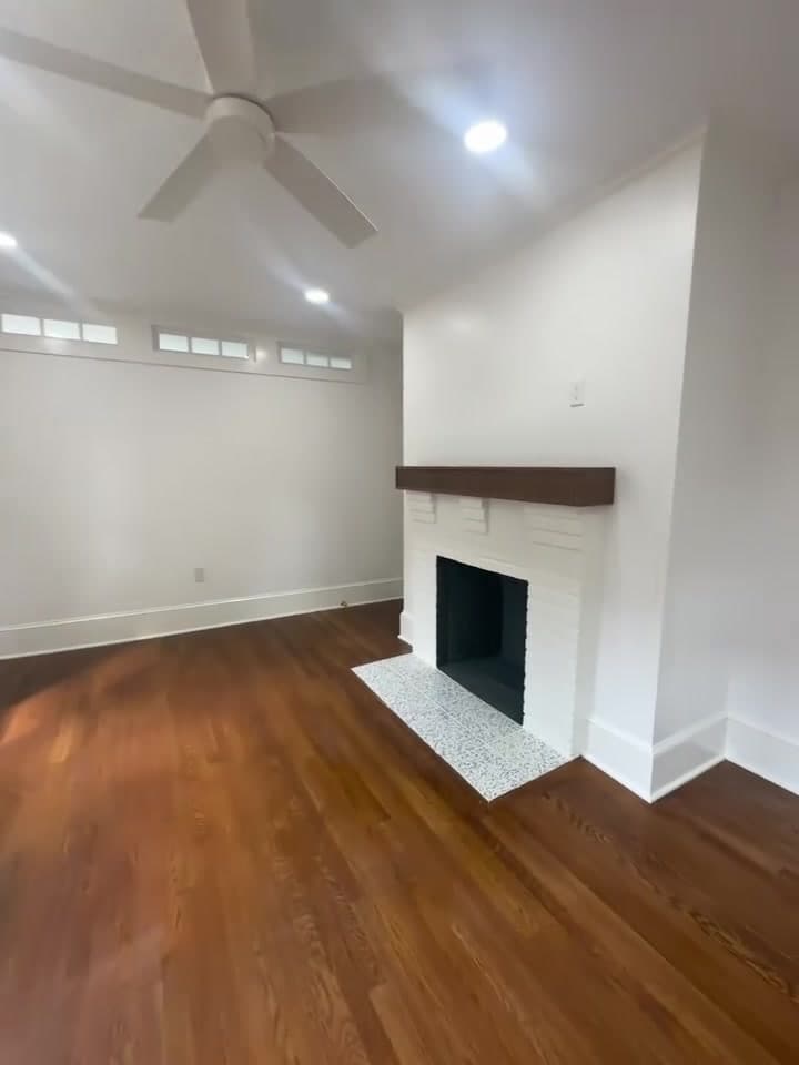 Renovated living room with a painted brick fireplace, wood mantel and hardwood floors