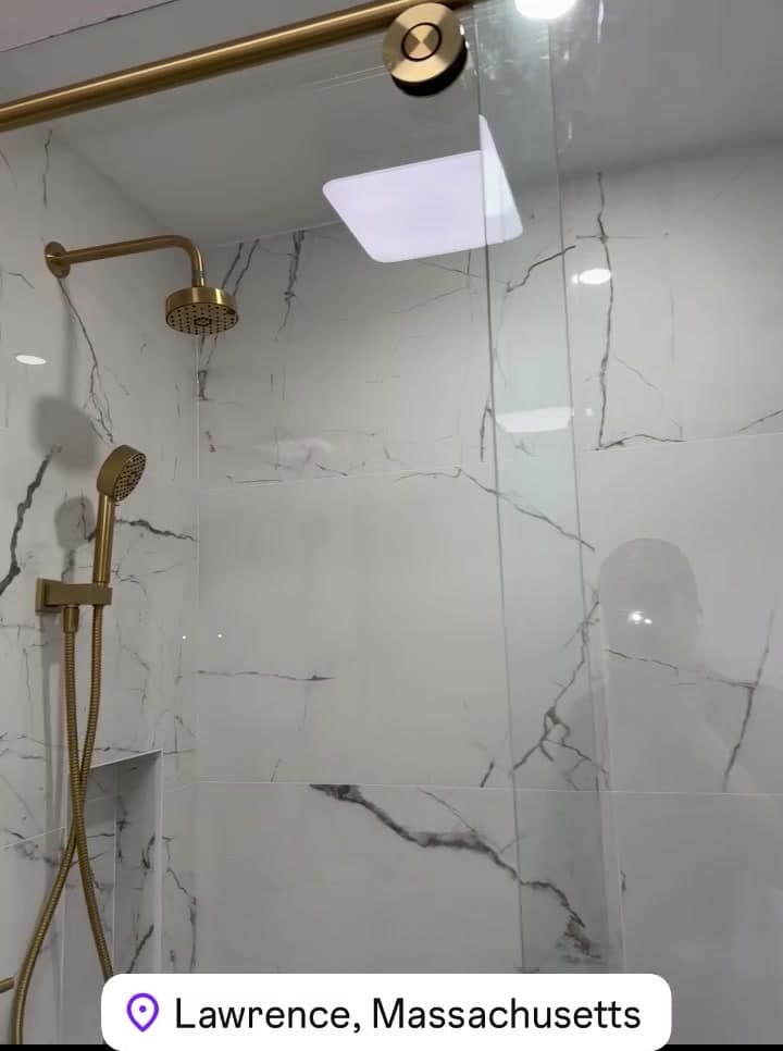 Walk-in shower with marble-look tile, brass fixtures and a glass door