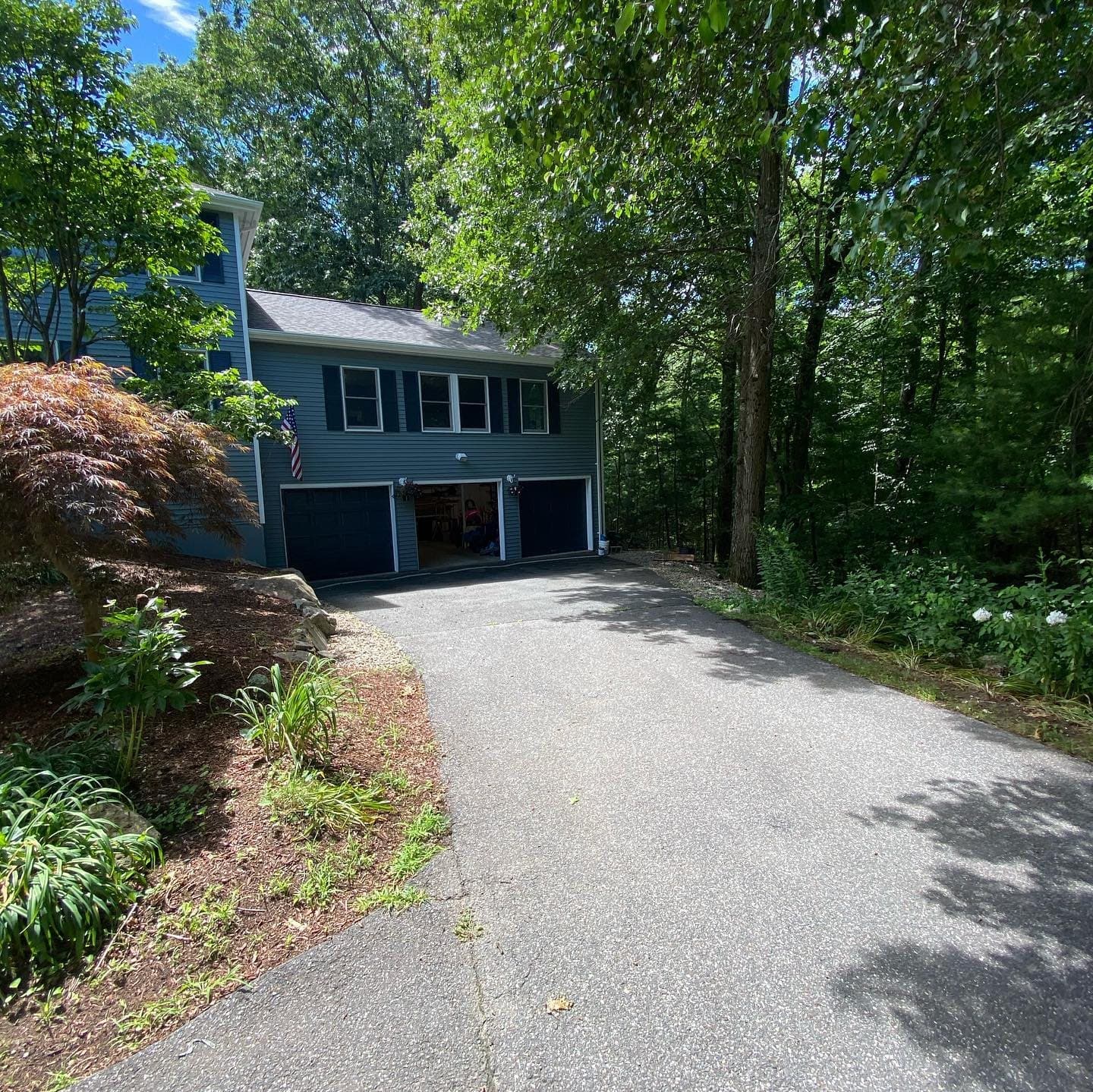 Blue-sided home at the end of a wooded driveway
